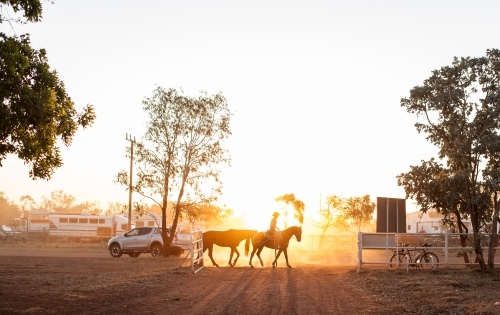 Golden light shining on cowboy riding horse - Australian Stock Image