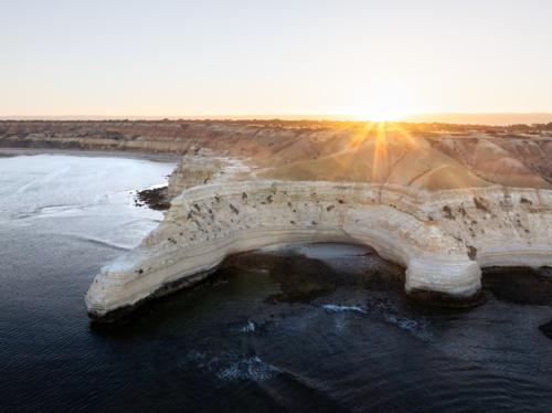 Golden light spills over the rugged coastline with layered limestone cliffs at sunset - Australian Stock Image