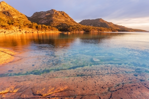 Golden lighting on coastal mountains behind calm water in large rock pools
