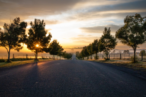 Golden rays of the morning sun on a country road on a moody country morning - Australian Stock Image