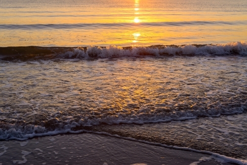 Golden reflections at water's edge at dawn with small waves - Australian Stock Image