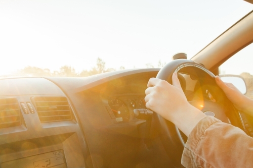 Golden sunlight flare over steering wheel and hands of car driver