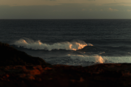 Golden sunlight illuminating ocean waves near rocky shore - Australian Stock Image