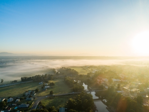 Golden sunlight over river with mist at the edge of town in morning light - Australian Stock Image