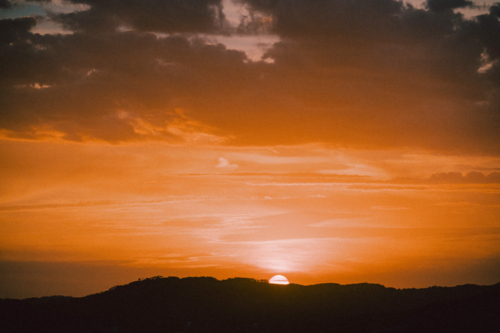 Golden sunset dipping below distant hills beneath dramatic clouds - Australian Stock Image