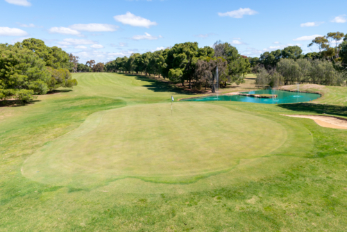 Golf course green and bunkers on a sunny day, surrounded by trees and blue sky - Australian Stock Image