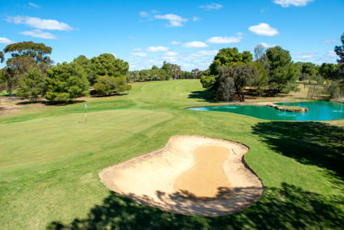 Golf course green and bunkers on a sunny day, surrounded by trees and blue sky - Australian Stock Image