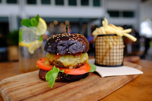 Gourmet burger in black brioche bun served with chips on a platter at a trendy cafe - Australian Stock Image