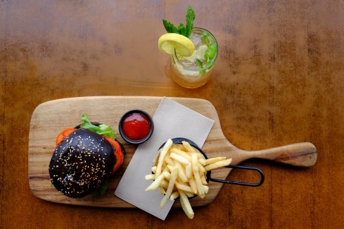 Gourmet burger in black brioche bun served with chips on a platter at a trendy cafe