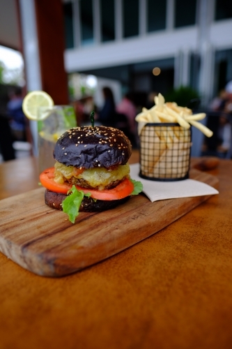 Gourmet burger in black brioche bun served with chips on a platter at a trendy cafe