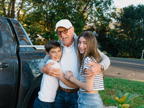 Grandfather embracing grandchildren outside the house. - Australian Stock Image