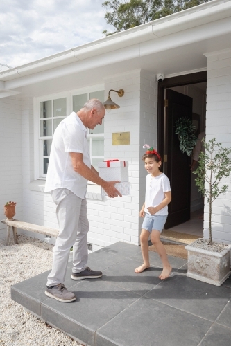 Grandfather giving Christmas presents to grandson on front porch - Australian Stock Image