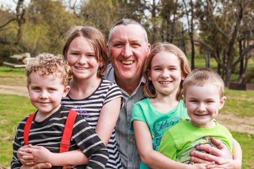 Grandfather sitting with grandchildren smiling - Australian Stock Image