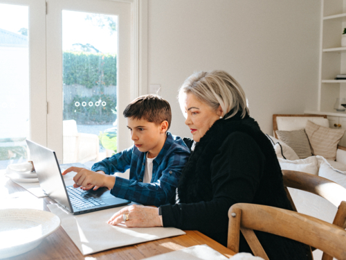 Grandma sitting with her grandson in front of a laptop on the table. - Australian Stock Image