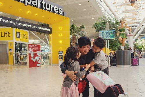 Grandmother and grandchildren hugging and saying goodbye at departures gate at an airport - Australian Stock Image