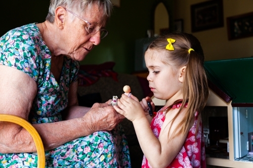 Grandmother and granddaughter playing with dollys in doll house