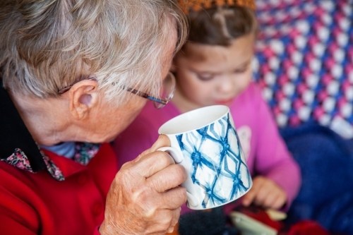 Grandmother holding mug of tea talking to granddaughter - Australian Stock Image