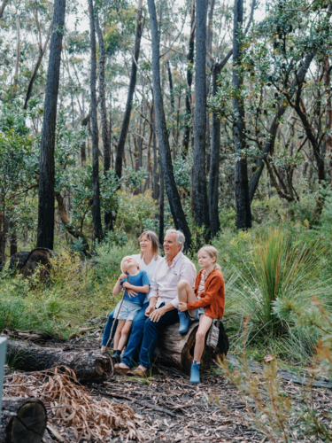 Grandparents enjoying Australian Bushland with their Grandchildren sitting on log together - Australian Stock Image