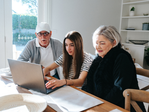 Grandparents sitting with their granddaughter in front of a laptop on the table. - Australian Stock Image