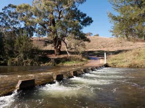 Gravel road with water running over concrete causeway - Australian Stock Image
