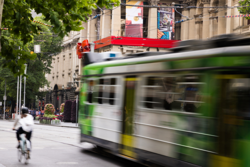 Green and white tram rushes past on a city street captured with motion blur - Australian Stock Image