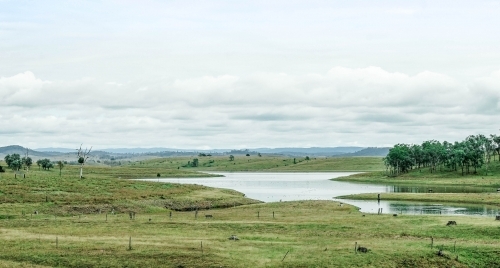 Green farmland with a lake and mountain view - Australian Stock Image