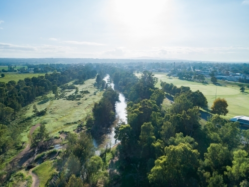 Green riverside grass sparkling from dew in morning light with sun shining on river water - Australian Stock Image