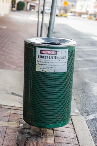 Green rubbish bin on street with litter notice