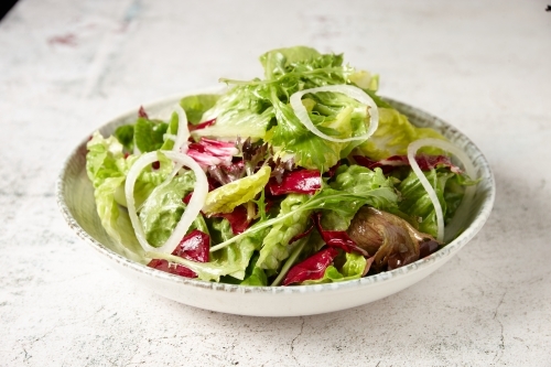 green salad in a bowl on top of a rustic grey tabletop with onion rings - Australian Stock Image