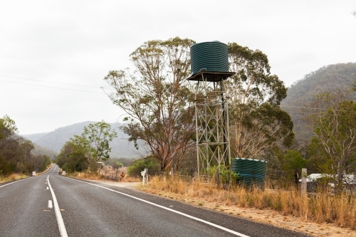 Green water tank on a stand on farm beside road - Australian Stock Image