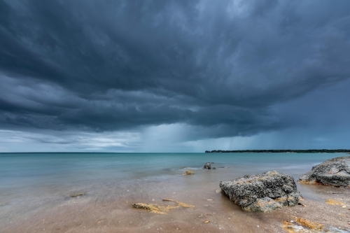 Grey storm clouds overhead with rain falling in the distance over the ocean - Australian Stock Image
