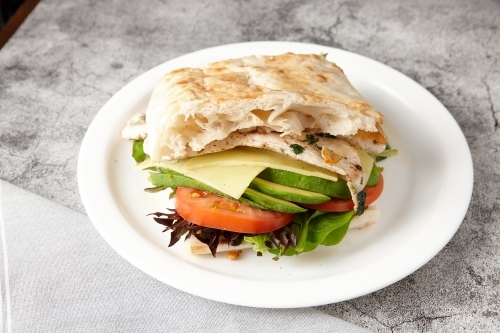 Grilled chicken and avocado focaccia in a white plate on a concrete surface. - Australian Stock Image