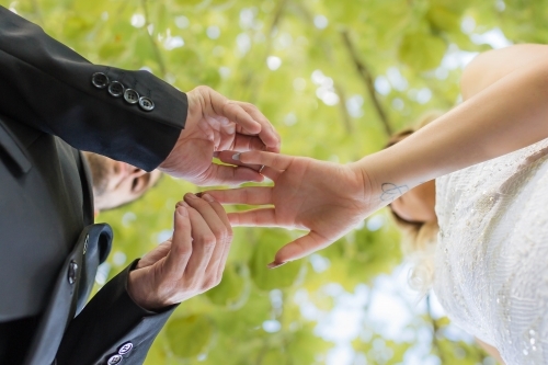 Groom putting ring on bride from underneath - Australian Stock Image