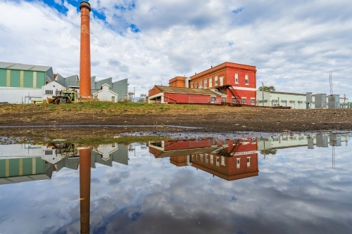Ground level view of a brick chimney at a  factory and its reflection in a puddle - Australian Stock Image