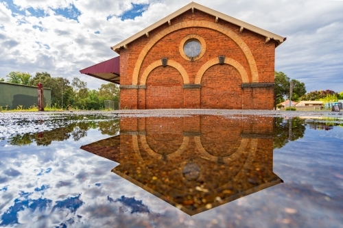 Ground level view of ornate brickwork on goods shed and its reflection in a puddle - Australian Stock Image