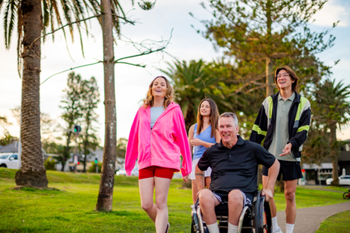 Group of four friends, including a man in a wheelchair, enjoying a lively afternoon in a park - Australian Stock Image