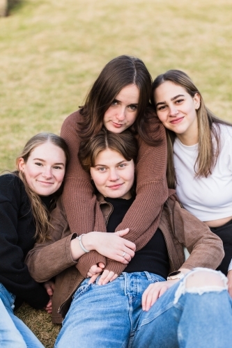 Group of four girls snuggled together sitting on grass smiling - Australian Stock Image