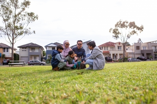 Group of people with man woman three children and a cat sitting down on a big lawn - Australian Stock Image