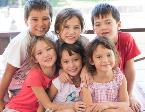 Group of Japanese-Australian siblings hugging one another closely smiling at camera. - Australian Stock Image