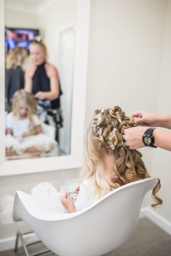 Hairdresser curling young girl's long blonde hair - Australian Stock Image