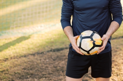 half body shot of a man holding a soccer ball while standing on the field - Australian Stock Image