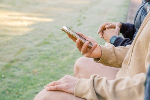 Half body shot of a man holding his cellphone wile sitting with a friend on his side - Australian Stock Image