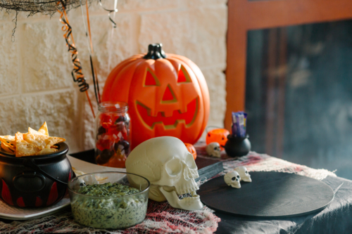Halloween-themed tabletop setup featuring a glowing jack-o’-lantern, decorative skulls, and snacks - Australian Stock Image
