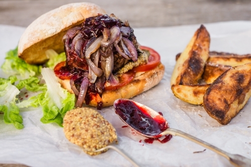hamburger with potato wedges and two spoons with mustard and relish - Australian Stock Image
