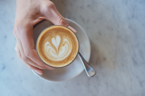 Hand holding a glass of coffee latte - Australian Stock Image