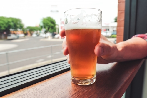 Hand holding glass of craft beer on window ledge over looking a street