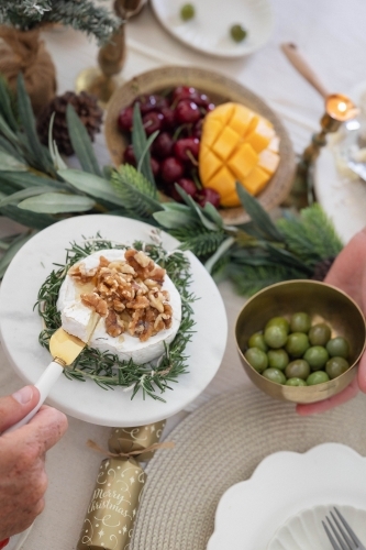 Hand lifting slice of camembert cheese at Christmas-decorated table - Australian Stock Image