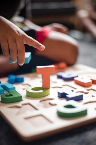 hand of Aboriginal boy playing with alphabet letter puzzle pieces - Australian Stock Image