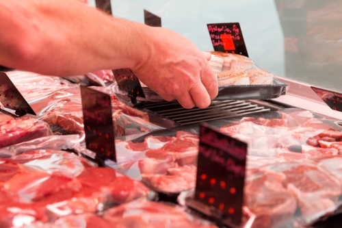 Hand placing meat on counter at butcher - Australian Stock Image