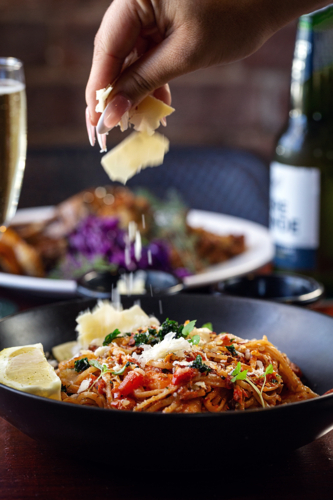 hand sprinkles grated cheese over a plate of pasta - Australian Stock Image